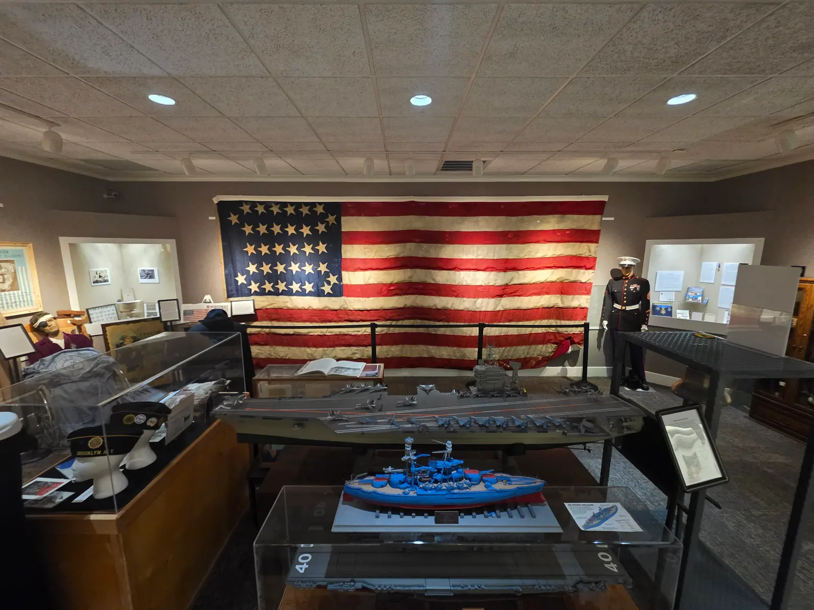 Scale models of an aircraft carrier and a battleship in glass cases, with the large flag behind them