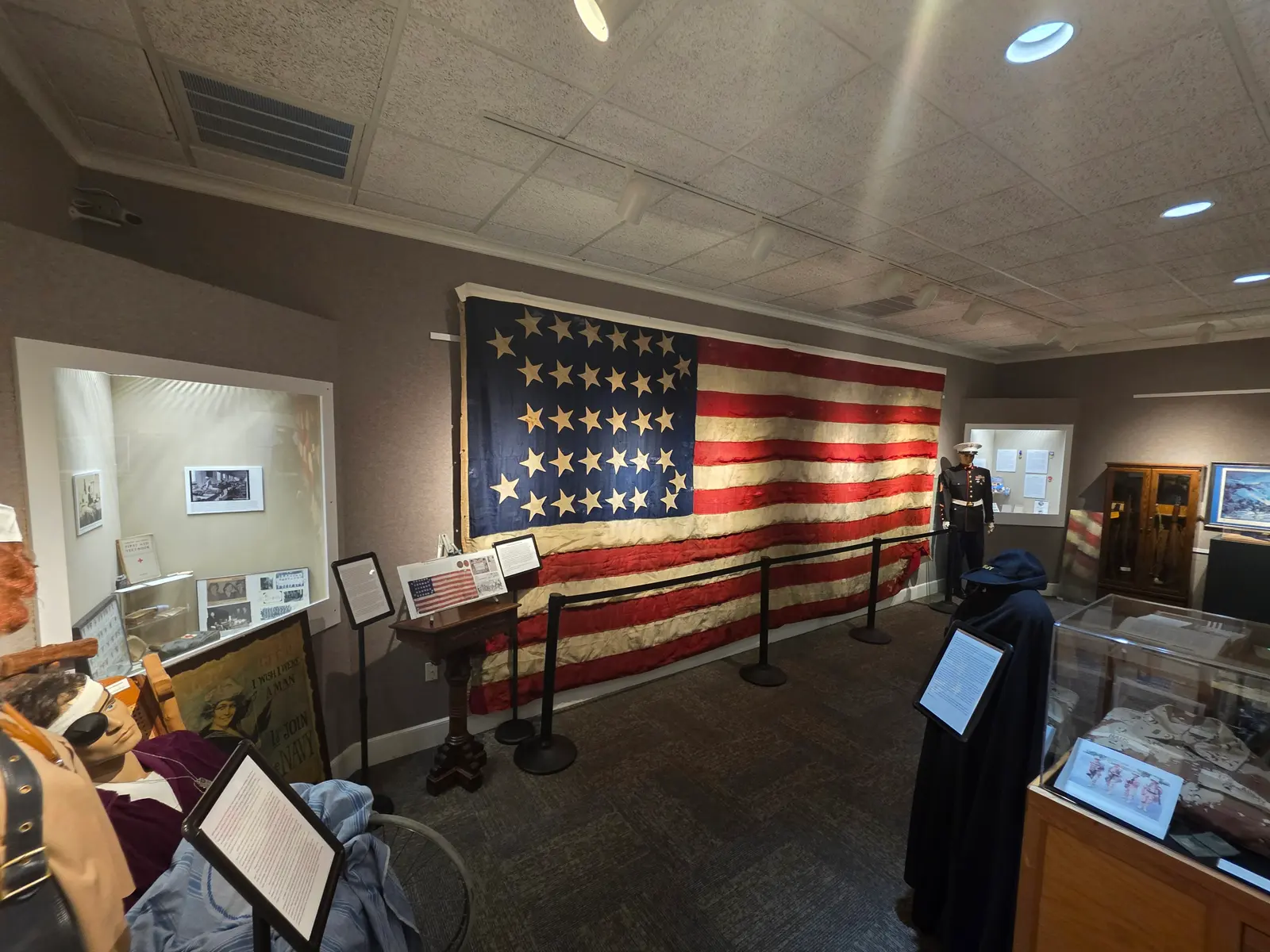 The Veterans History Museum gallery, with a large Civil War–era flag, a Marine in dress blues, uniforms and display cases