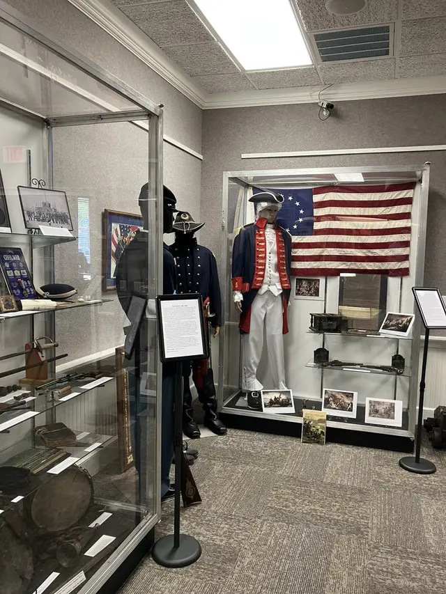 Mannequins in Union Army uniforms stand beside a glass case holding a red-and-blue colonial-style uniform, a tricorn hat and an early American flag